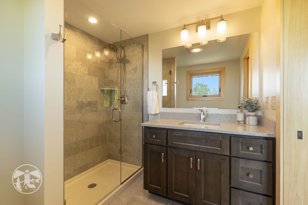 Modern bathroom renovation by Lighthouse Contracting Group in New Hampshire’s Lakes Region featuring a frameless glass shower, gray tile surround, dark vanity, and quartz countertop.